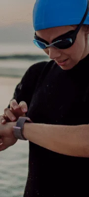 Mulher vestindo roupas de nadadora de neoprene, touca e óculos de natação. Olhando o relogio na praia.