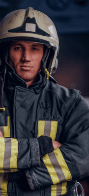 bombeiro vestido com macacão de segurança e capacete. De braços cruzados.