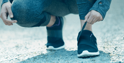 Pessoa agachada apertando o velcro do tenis. Vestindo roupas de caminhada e tenis preto.